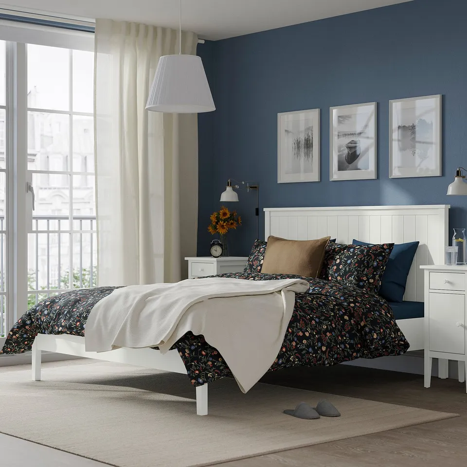 Modern bedroom with white GULLABERG bed and floral bedding. Includes bedside tables, a window, and blue wall with art.