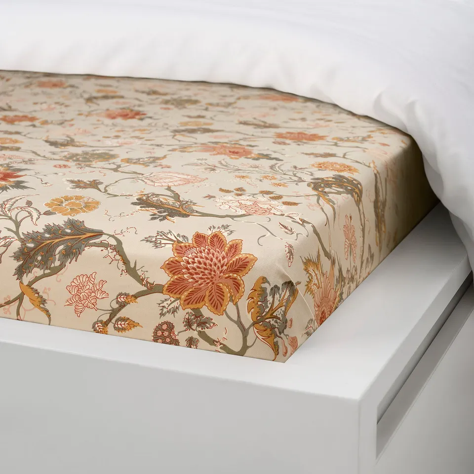 A bed with a beige floral-patterned fitted sheet, showcasing its elastic edge designed to fit mattresses up to 26 cm thick.
