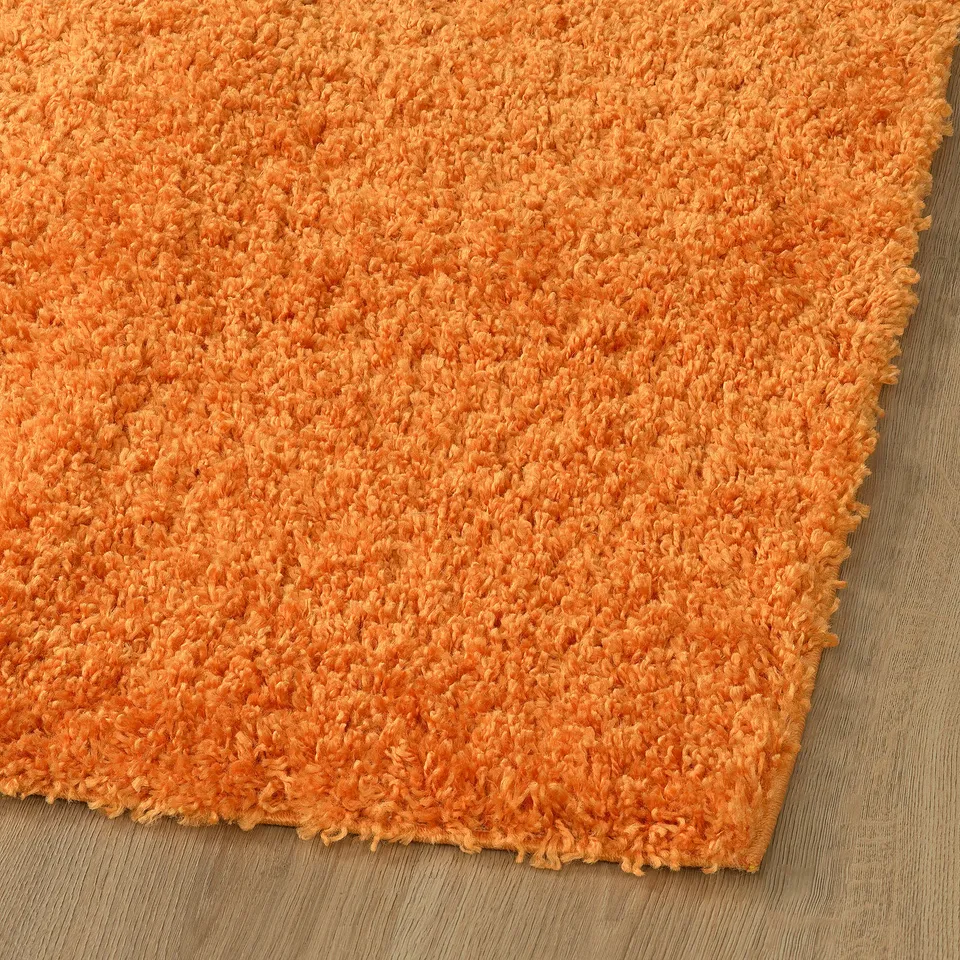 Thick, plush orange rug with soft texture, providing warmth and comfort. Ideal for living spaces, with stain-resistant and sound-dampening qualities.