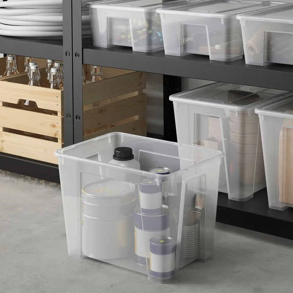 Clear plastic SAMLA boxes, various sizes, on metal shelves, some with cylindrical items, wooden crates nearby.