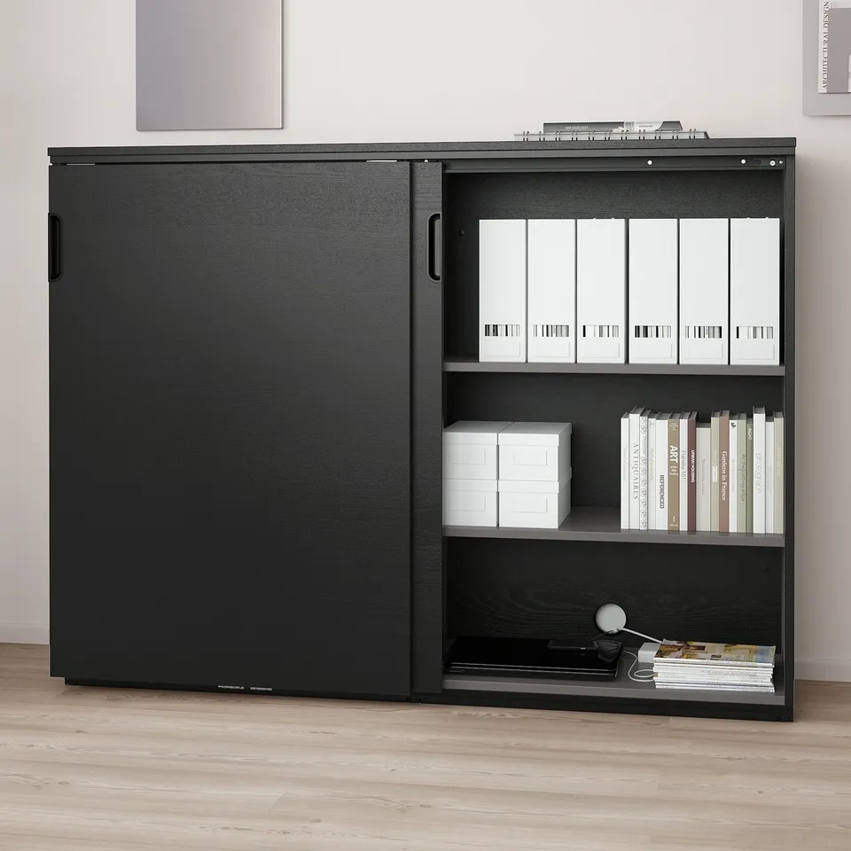 Black office storage cabinet with sliding doors and shelves. Adjustable shelves hold files and books. Locking mechanism for secure storage.