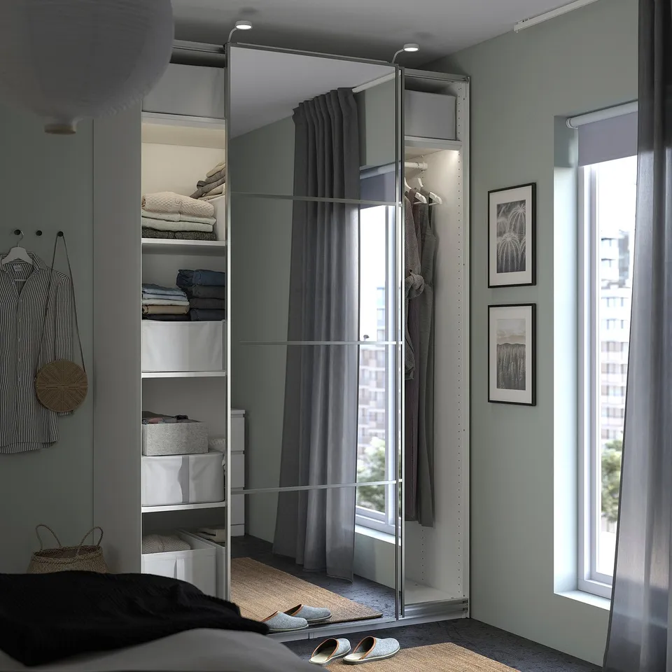 Modern bedroom with reflective sliding closet doors, organised storage, and minimalist decor.