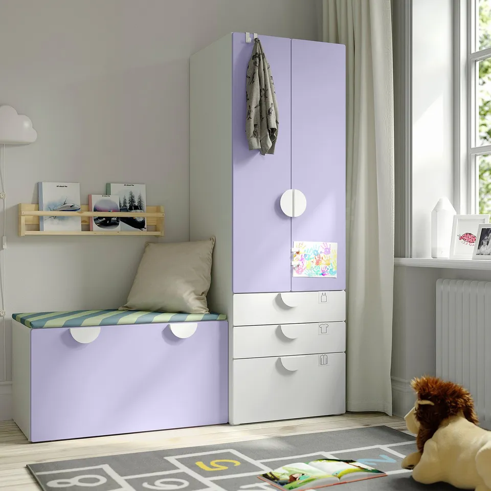 A kids bedroom featuring a tall, light purple and white SMÅSTAD storage unit with drawers and a bench, next to a window.