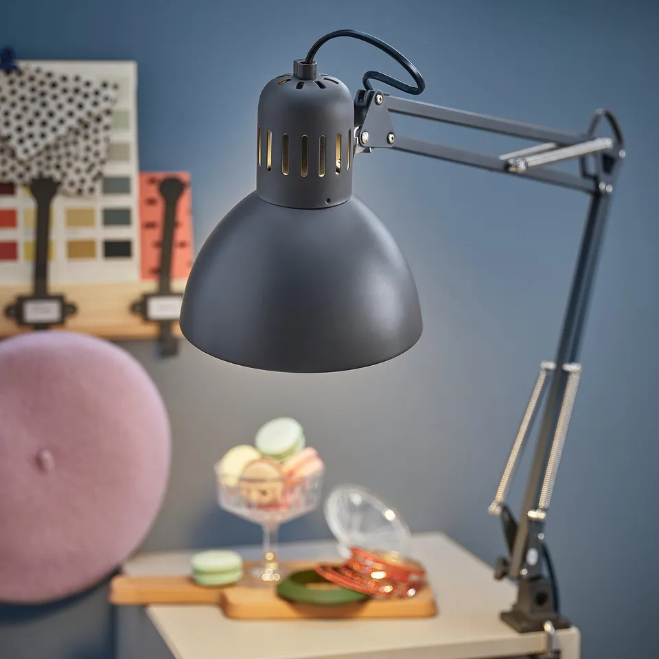 A sleek black modern desk lamp, TERTIAL, with adjustable arms and a dome-shaped shade, positioned on a table next to colourful cookies.