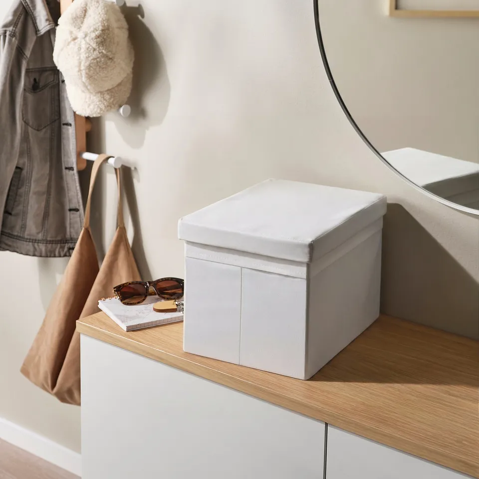 Grey lid on white box, beside bag, sunglasses, book, and mirror.