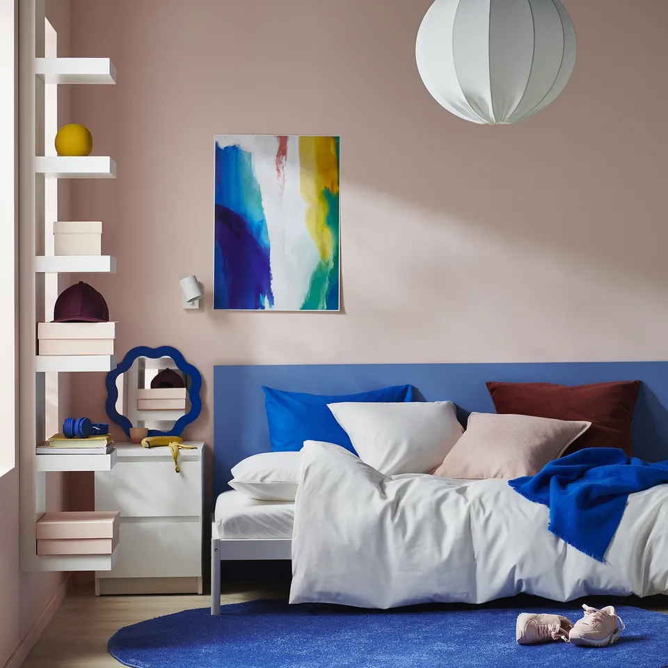 Modern blue twin bed with red bolster, white pillows, and colourful decor.