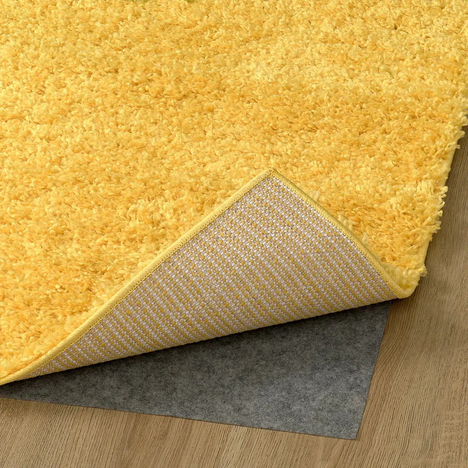 Yellow, shaggy rug with a white, textured backing attached to a grey non-slip mat on a wooden floor.