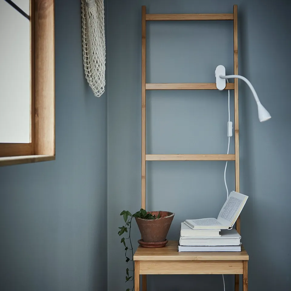 Reading nook with ladder shelf, lamp, book, plant.