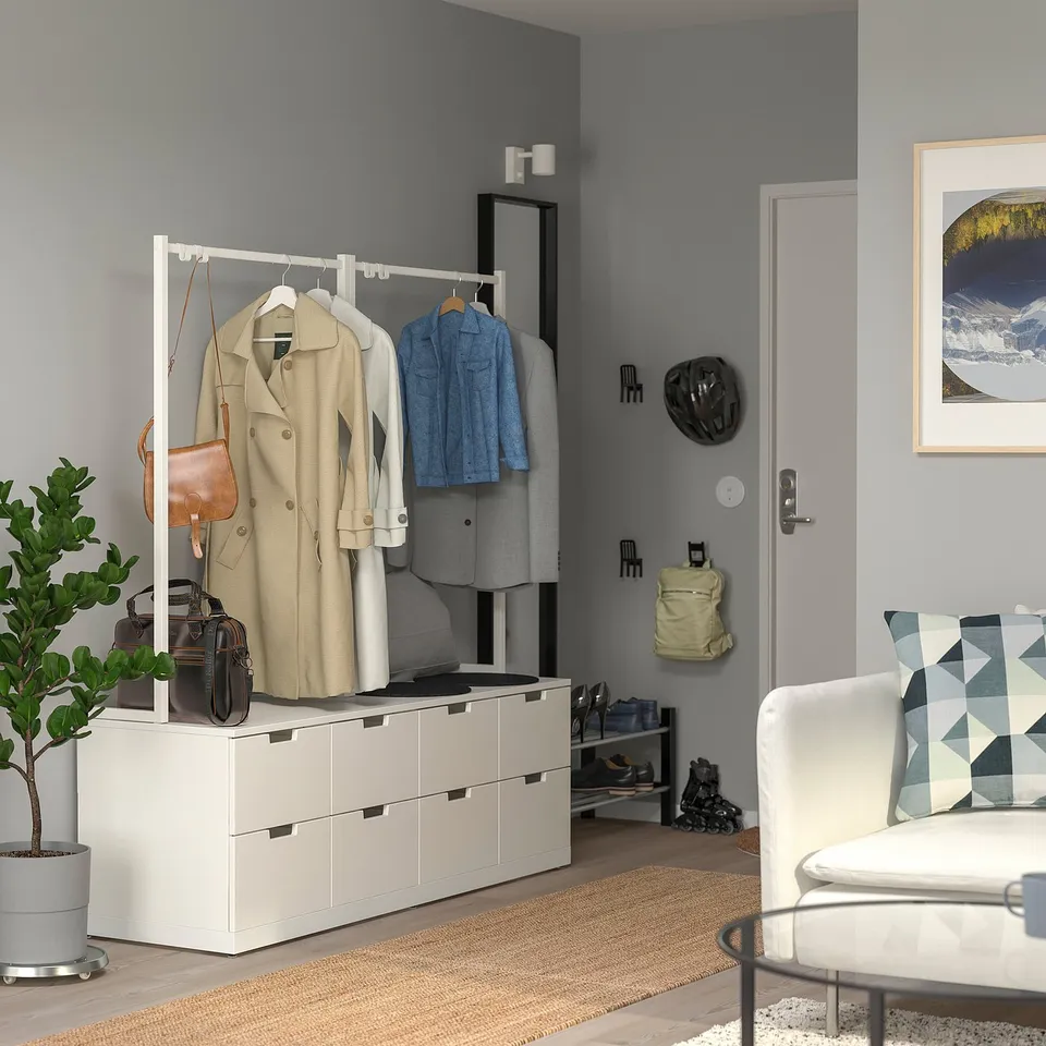 A modern grey NORDLI chest with drawers, hanging rail, and placed near an entry door, smaller than a sofa.
