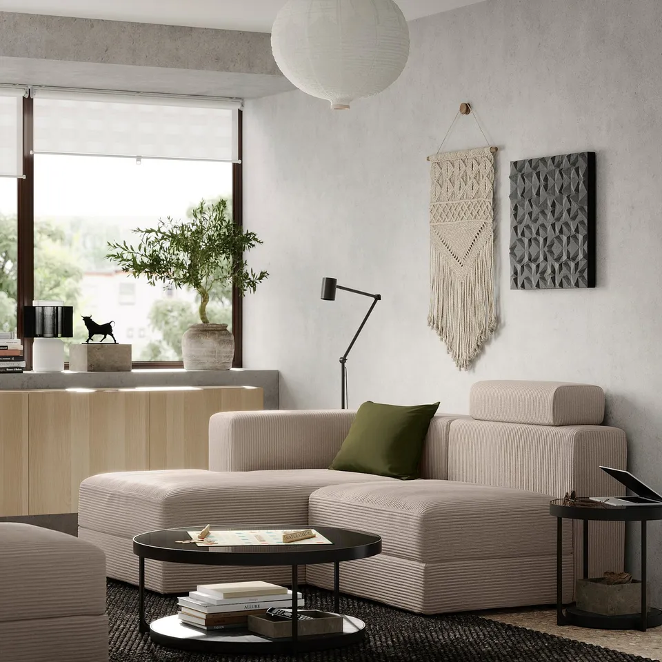 Modern living room with beige JÄTTEBO sofa, green pillow, black coffee table, books, lamp, wall hangings, and large window.