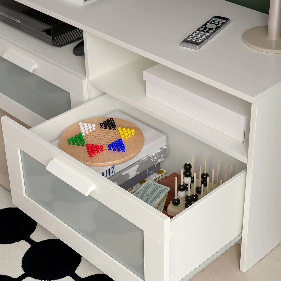 White tv stand with large open drawer full of colourful game pieces and puzzles, plus remote on top.