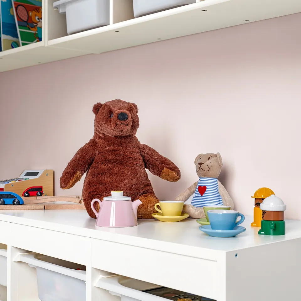 Playful kids shelf with DJUNGELSKOG teddy bears, colourful teacups, and a toy train; bear is large and brown.