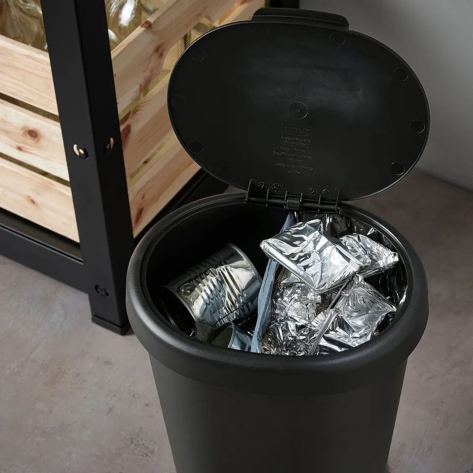 Black kitchen waste bin with lid open, showing crumpled silver foil inside.