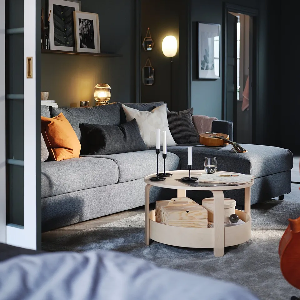 Modern living room with VIMLE grey sofa, orange cushions, wooden coffee table,arlamp, dark walls, white doors, black and white framed art.