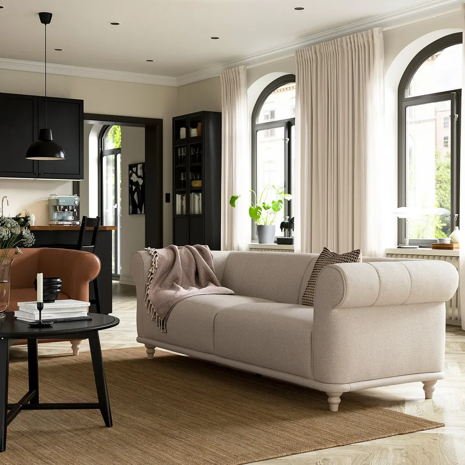 Modern living room with beige VISKAFORS sofa, brown rug, black side table, orange chair, and arched windows with white curtains.