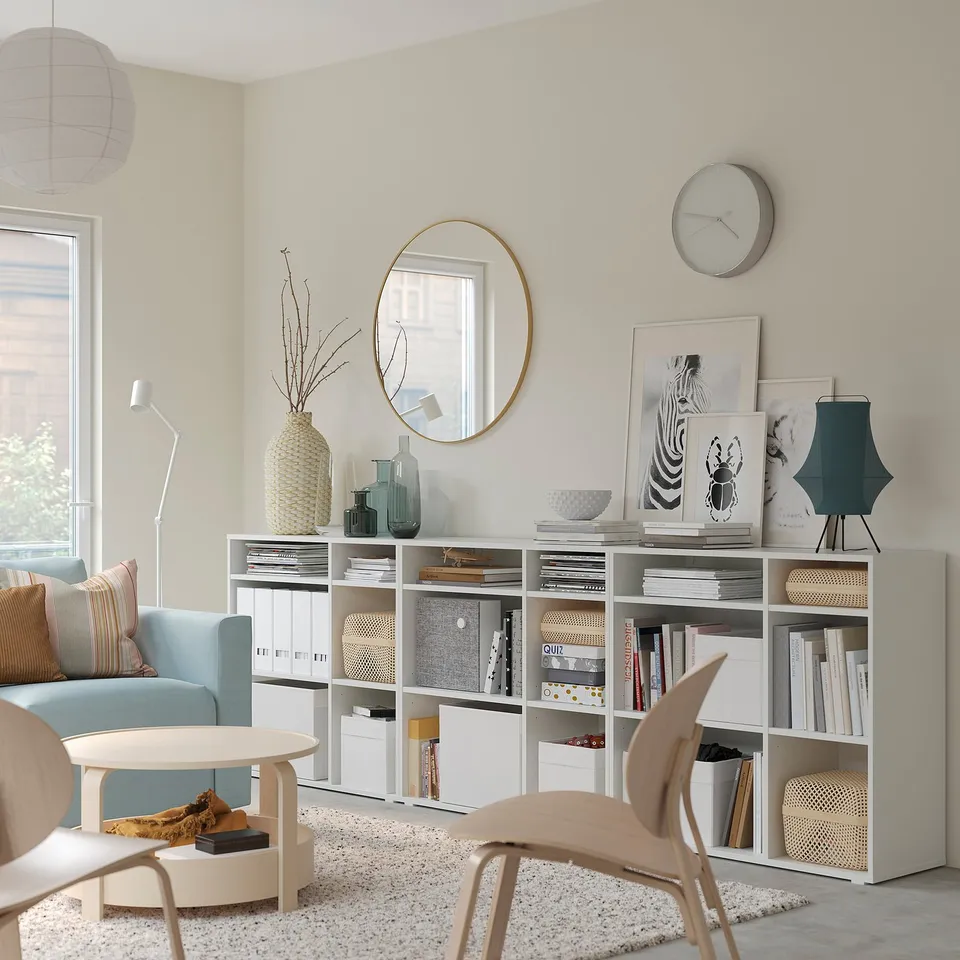 Modern living room with light blue sofa, white storage units, decorative items, and a circular mirror.