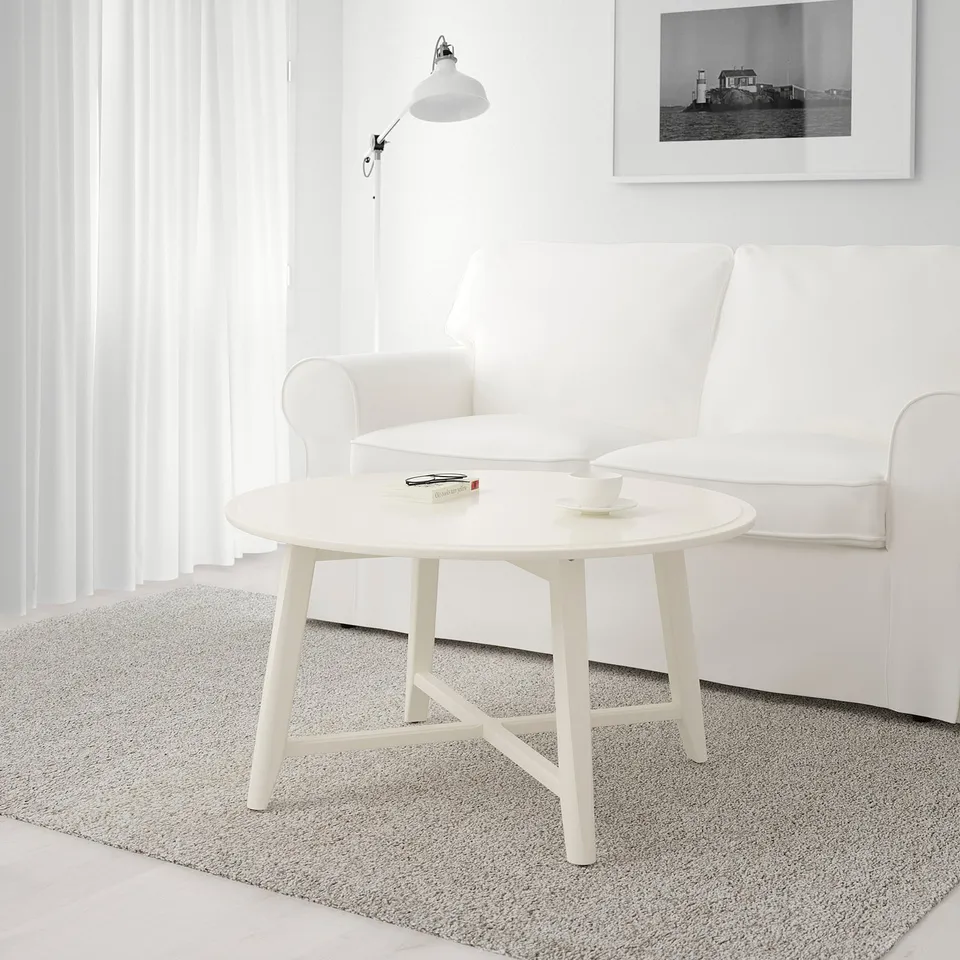 Minimalist living room a KRAGSTA coffee table with modern round design, placed before a white couch, holding a cup and remote on a plush area rug.