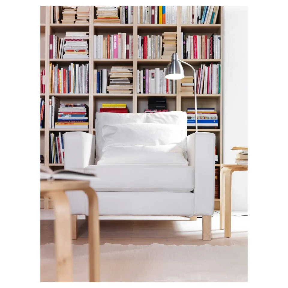 A cosy living area with a white LERSTA floor lamp beside a grey armchair, lit beside a bookshelf filled with colourful books.