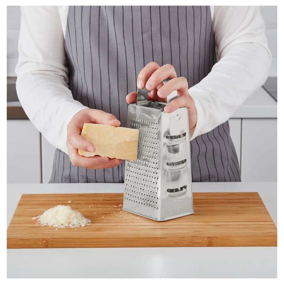 Person grates cheese using a silver box grater on a wooden cutting board.