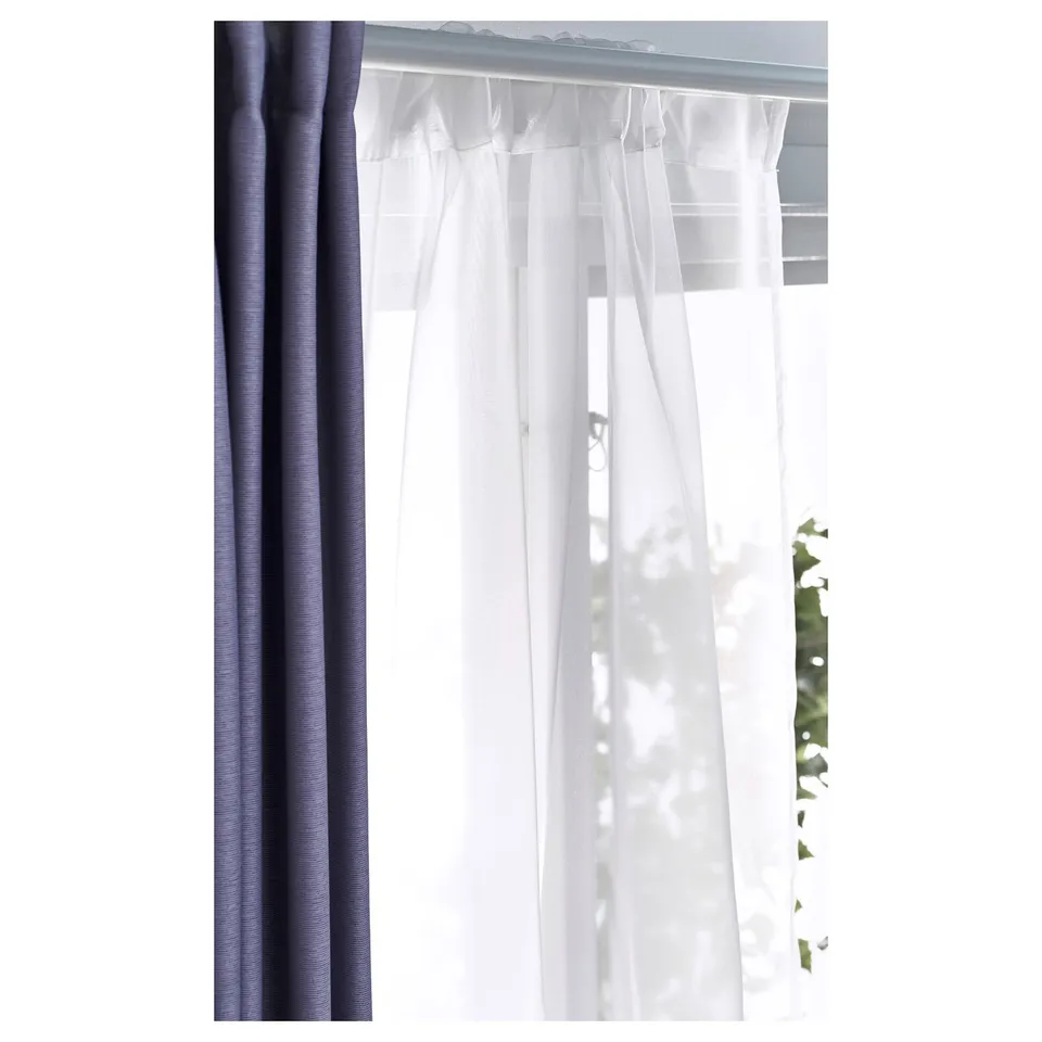 Sheer white curtains beside dark blue ones allow daylight and privacy, with visible rod system.