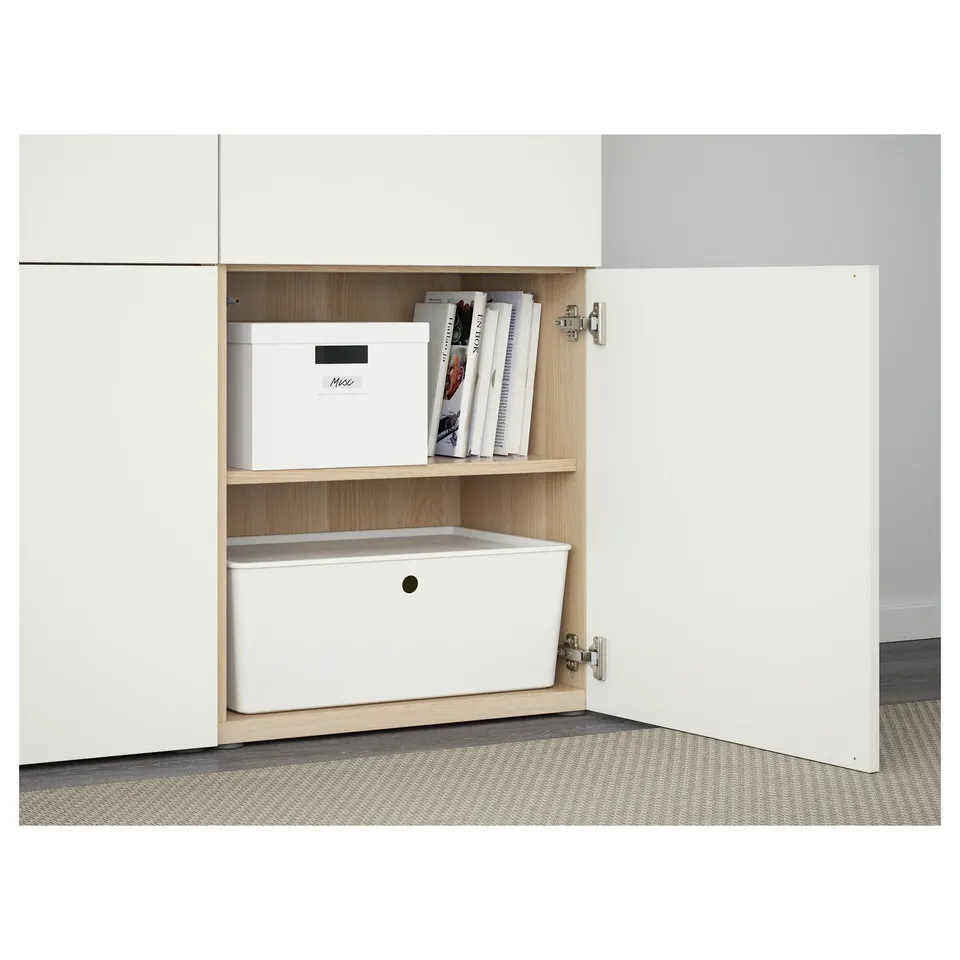 White cabinet with two shelves. Bottom shelf has a white bin, top shelf has a box and books. Hinges visible for soft-close/push-open functionality.