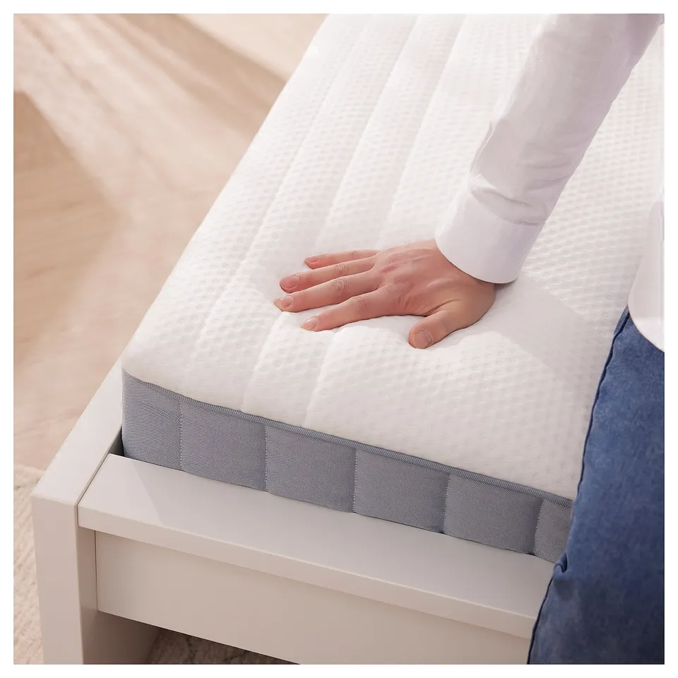 Person placing hand on a white VITMÅSEN mattress on a white bed frame.