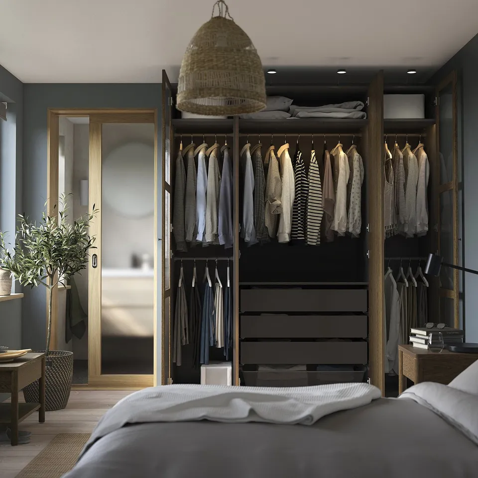 Modern bedroom with a grey bed, wardrobe, and a door. The open wardrobe displays clothes, shelves, and drawers.