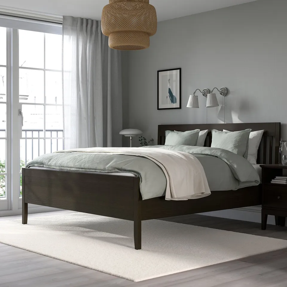 Modern bedroom with IDANÄS dark brown wooden bed, light blue walls, white linens, hanging pendant lamp, and large window with curtains.