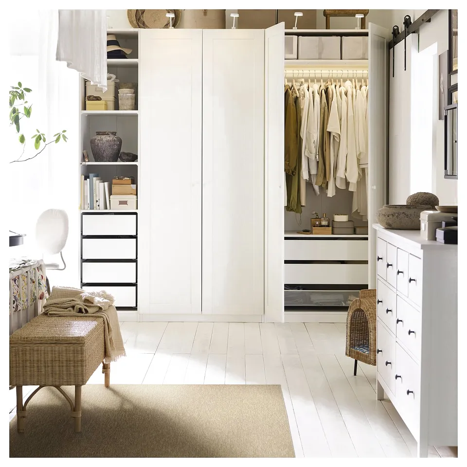 Modern bedroom featuring LÄTTBETONG rug, white floors, and furniture. Clothes on hangers, books, and decorative items visible.