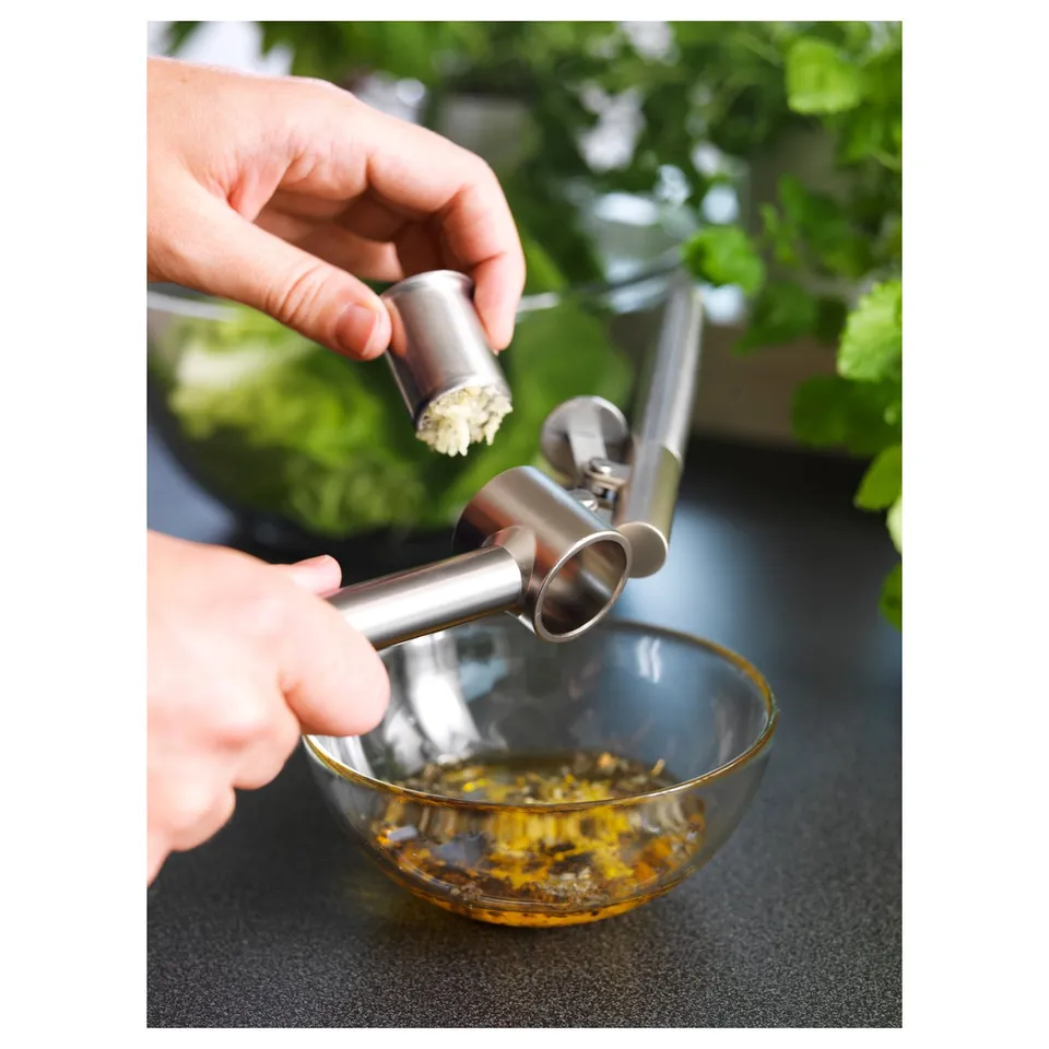 Using garlic press to mince cloves into bowl.