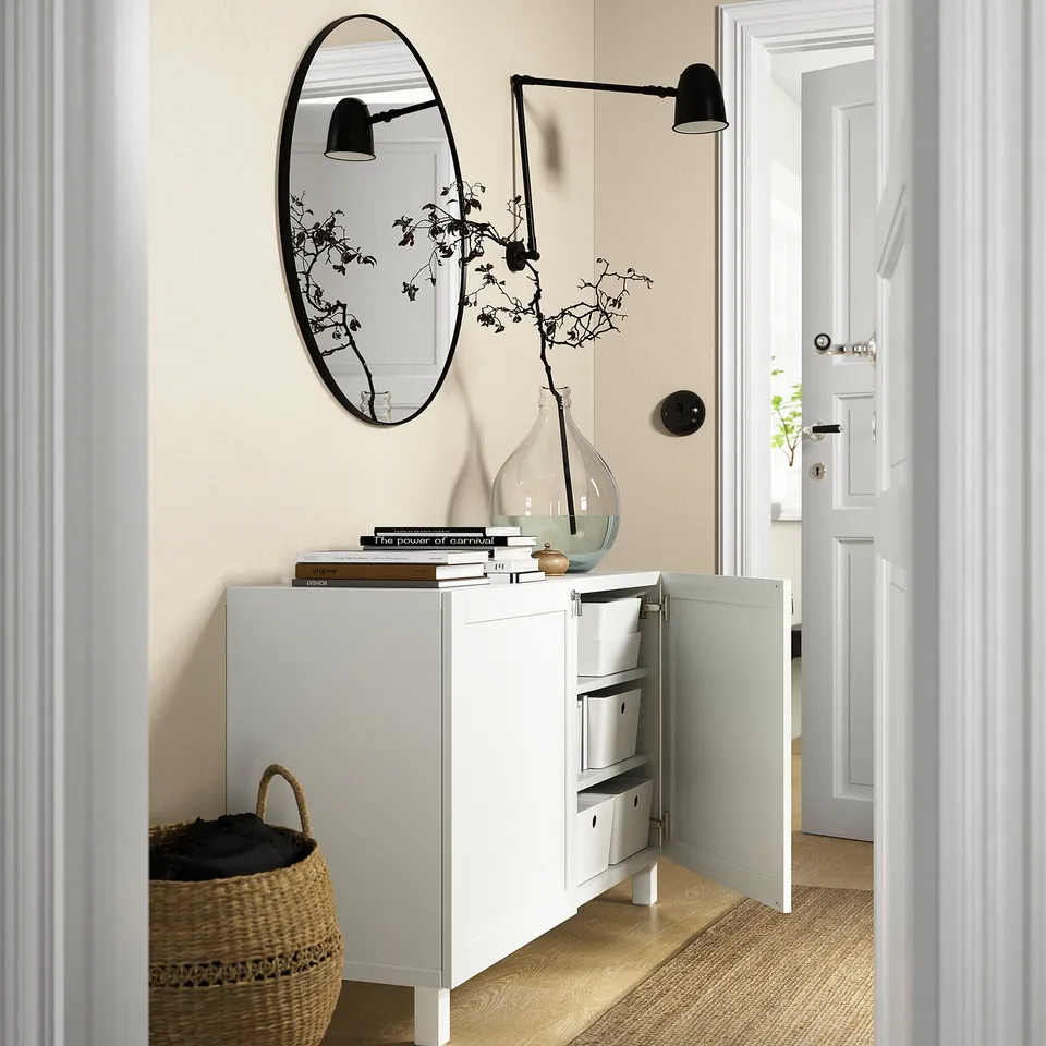 Modern hallway with white BESTÅ storage unit. It has adjustable shelves and soft-close doors. Decorated with books and a vase.