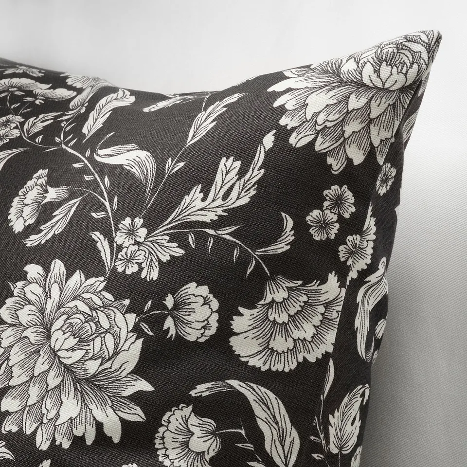 Black pillow with white floral design, intricate details, smooth fabric, seen from side.