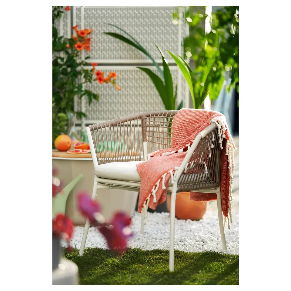 Wicker outdoor chair with red blanket, plants, and decorative table.