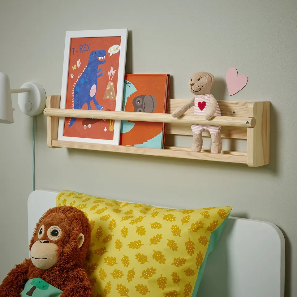 Kids room with green walls, books, teddy bear, and toys on a wooden shelf. White bed with turtle pillows completes cosy decor.