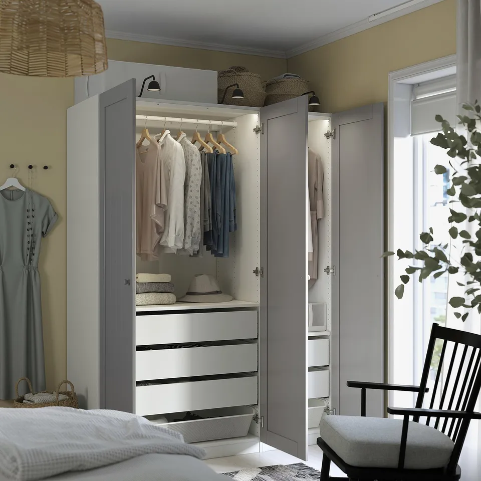 A modern bedroom with an open grey PAX wardrobe displaying clothes, drawers, and interior storage solutions.