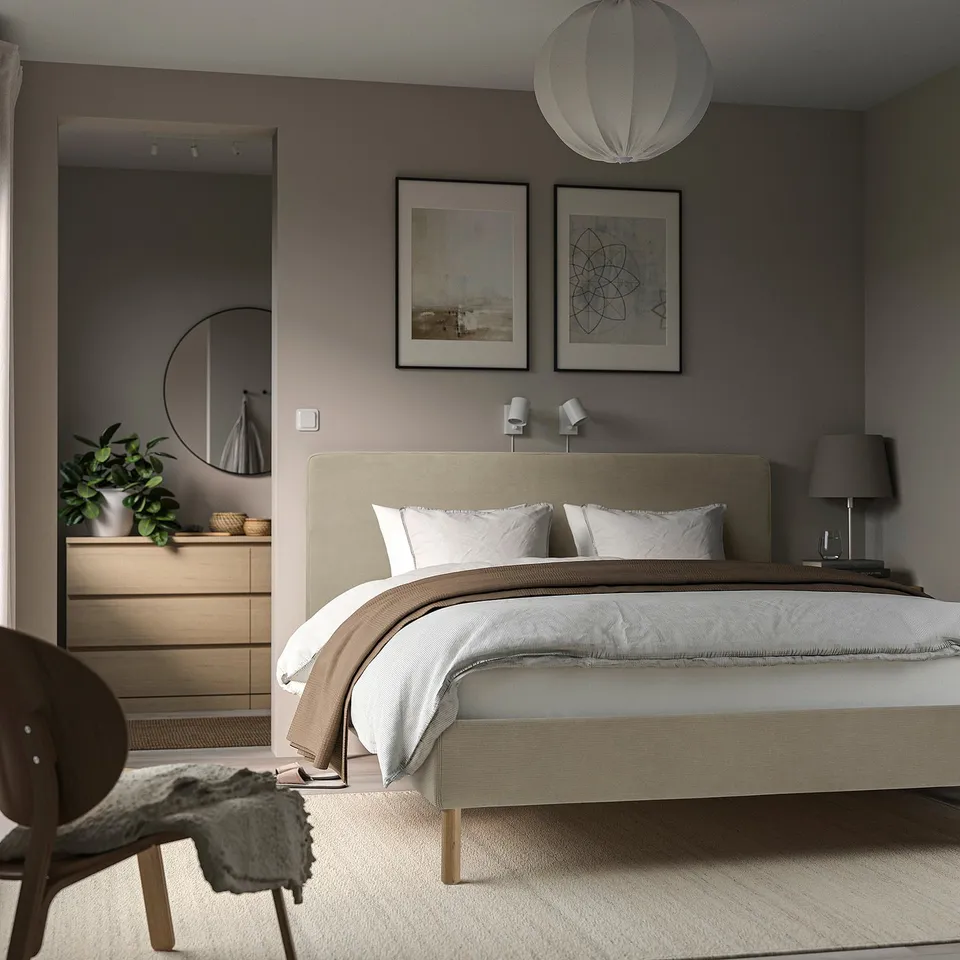 Modern bedroom with TÄRNKULLEN bed, white linens, artwork, mirror, dresser, lounge chair, rug, and hanging light.