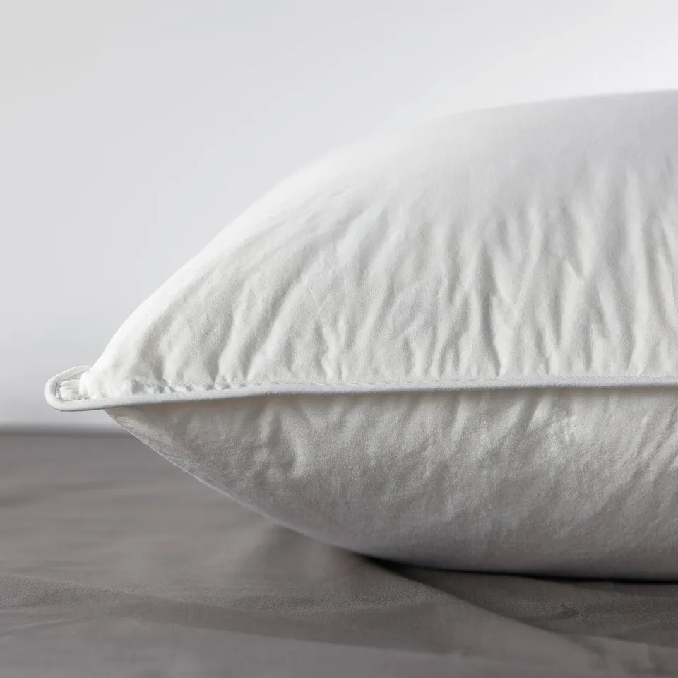 Close-up of a high-quality, soft pillow on a bed. The pillow is plump, with visible down feathering. It looks comfortable for side or back sleepers.