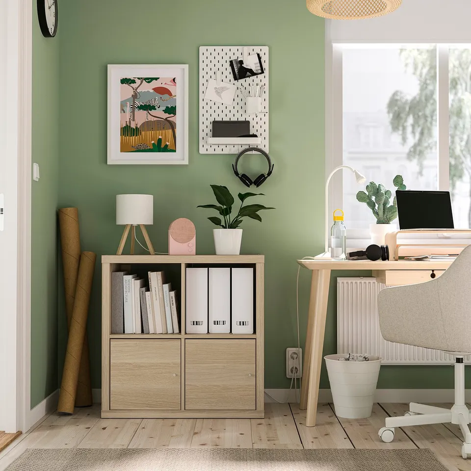 Home office with wall-mounted KALLAX storage, books, plant, and computer desk by green walls.
