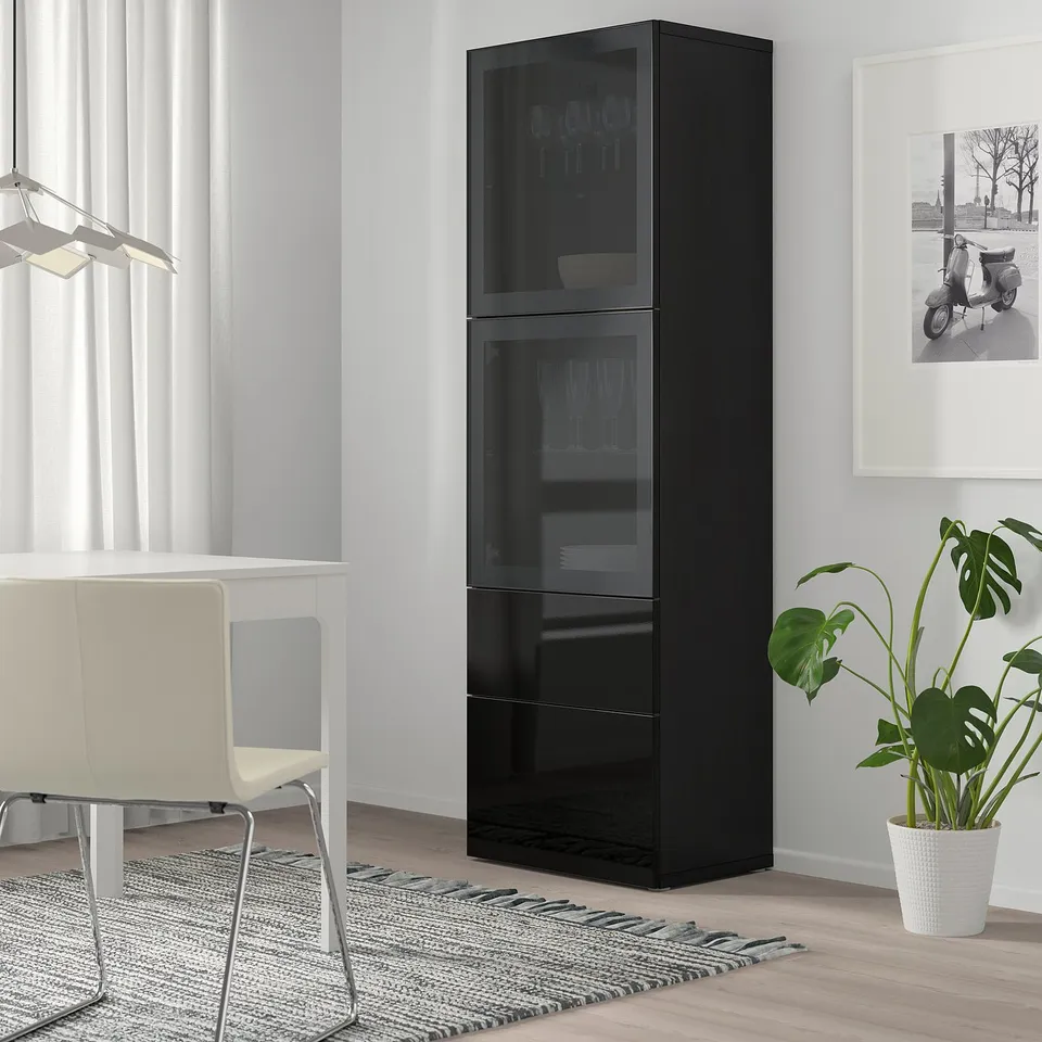 Modern living room: black BESTÅ cabinet with glass shelves, white chair, large plant, minimalistic design.