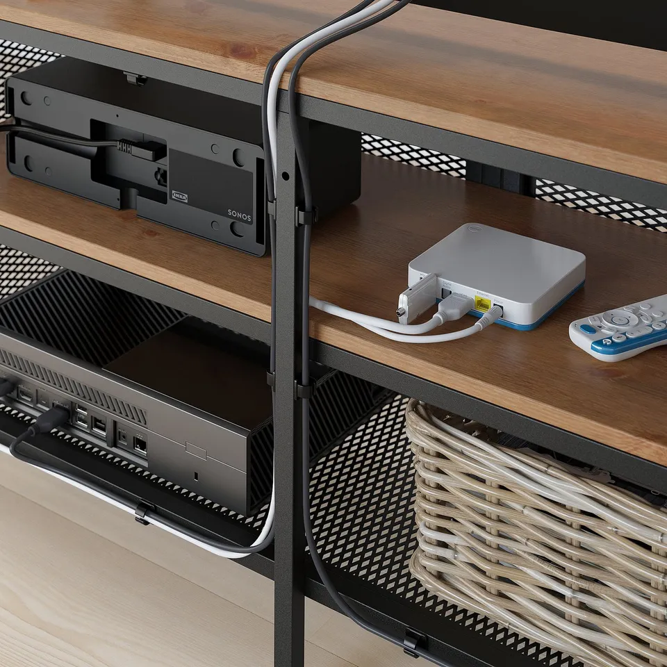A wooden tv stand with metal mesh doors and cable management, housing a media player and remote controls.