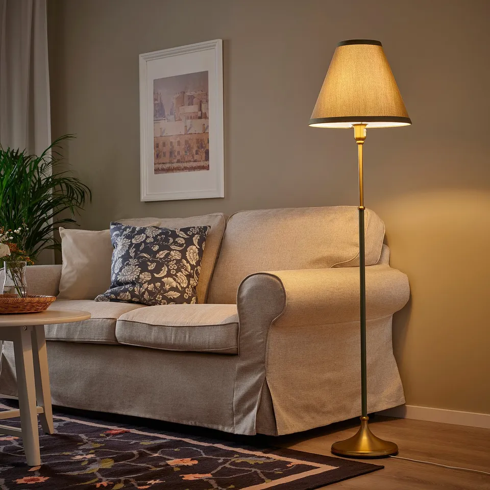 Beige FLYGHÖJD lamp beside light sofa with cushions, framed picture, plant table.