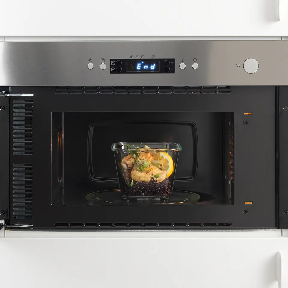 Modern microwave oven with digital display and glass container of food inside, ready to be heated.