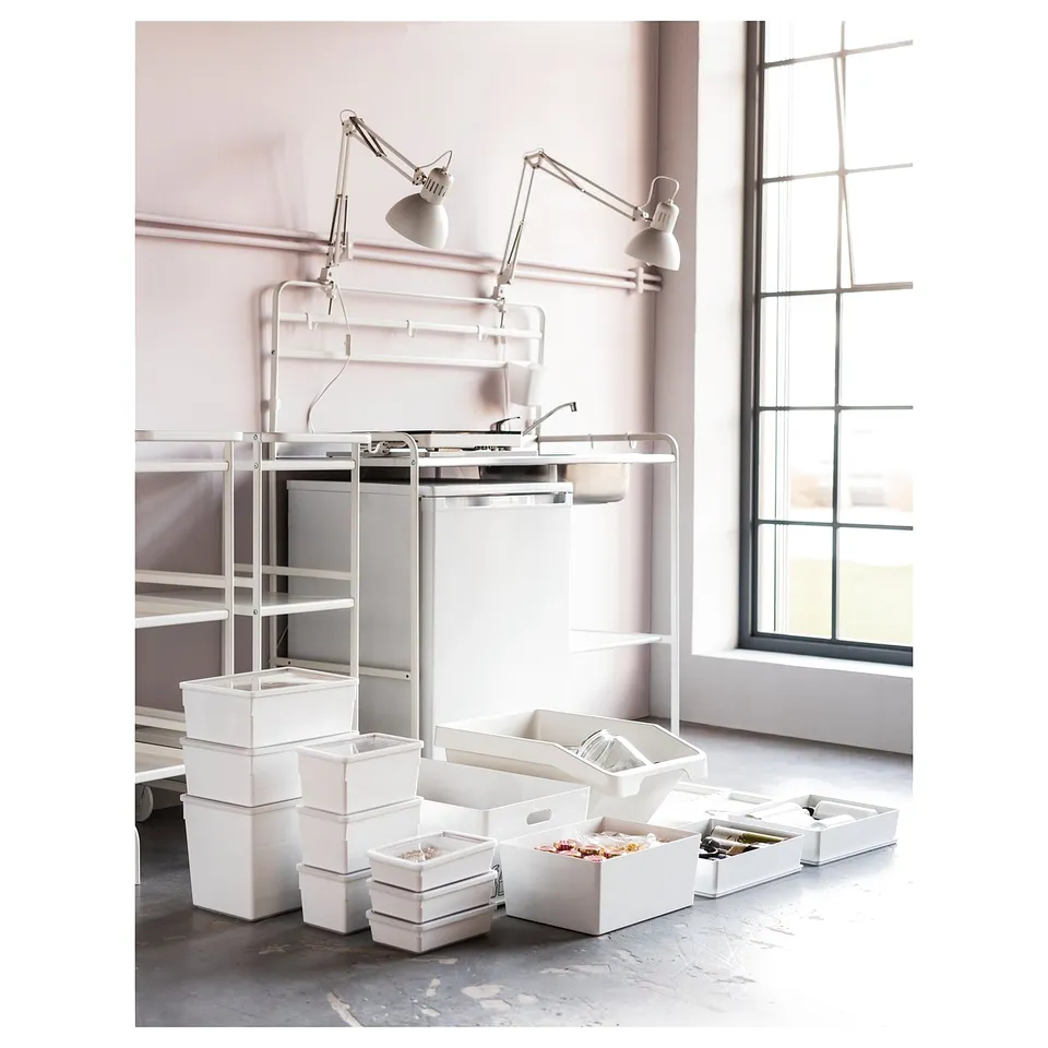 Modern white mini-kitchen with metal shelves, sink, adjustable lamps, and organised storage.