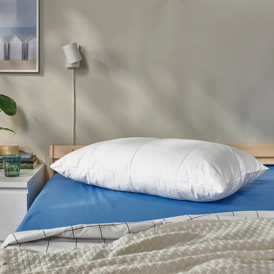 White SENAPSMOTT pillow on bed with blue sheets and lamp.