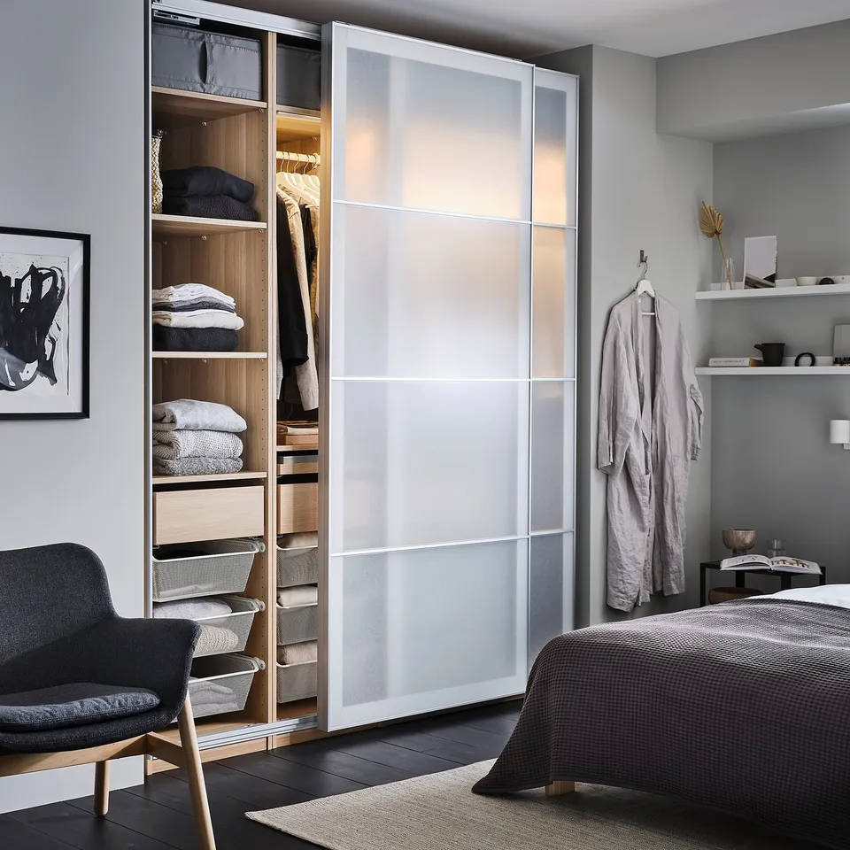 Modern bedroom with PAX wardrobe, featuring frosted glass doors, wooden interior, and organised compartments for clothes.