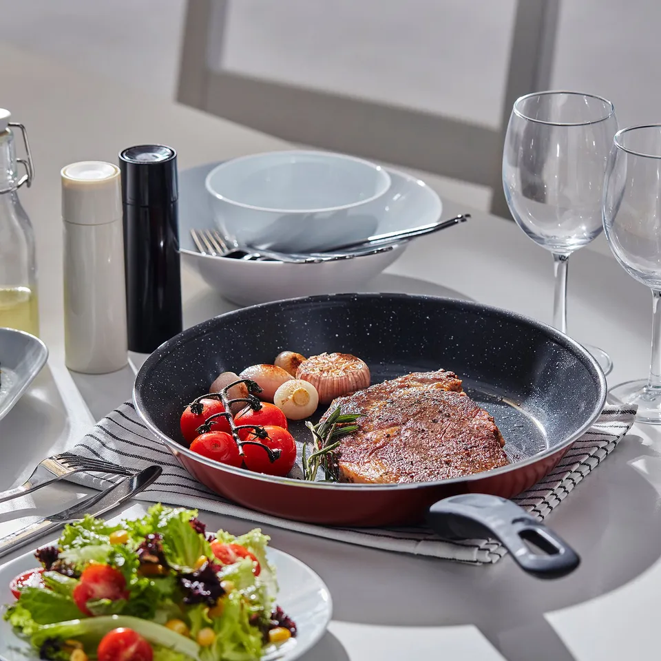Table setting with steak, veggies, salad, and glasses. Non-stick frying pan with seasoned steak, tomatoes, and mushrooms.