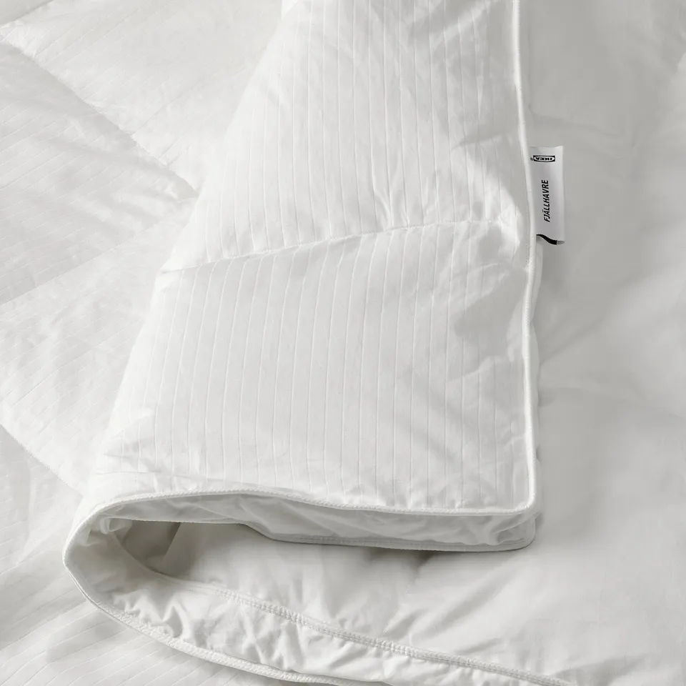A fluffy white duvet on a bed, with a tag showing the brand FJÄLLHAVRE indicating soft, down-filled warmth.