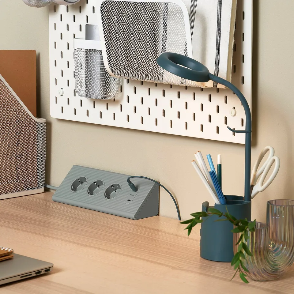 Wooden desk with adapter, lamp, pens, plant, headphone hooks.