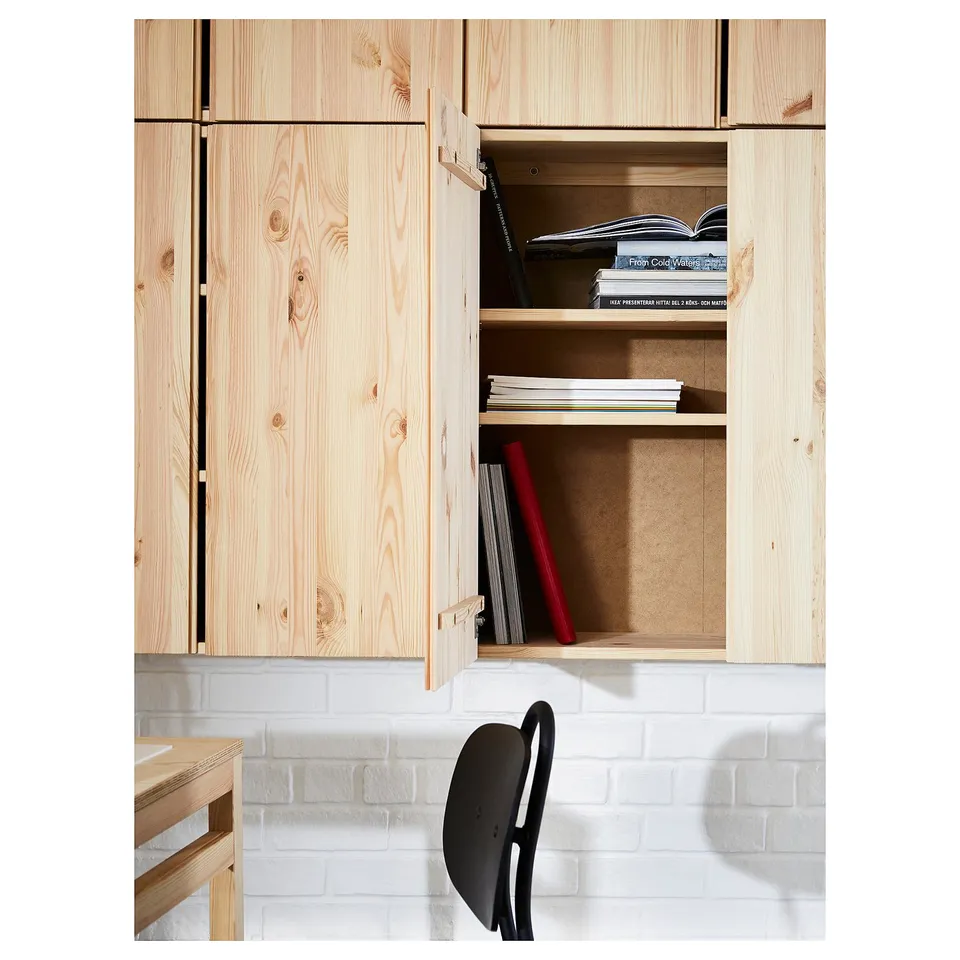 Light wood cabinet with open door revealing books and a red box, against a white brick wall; minimalist design.