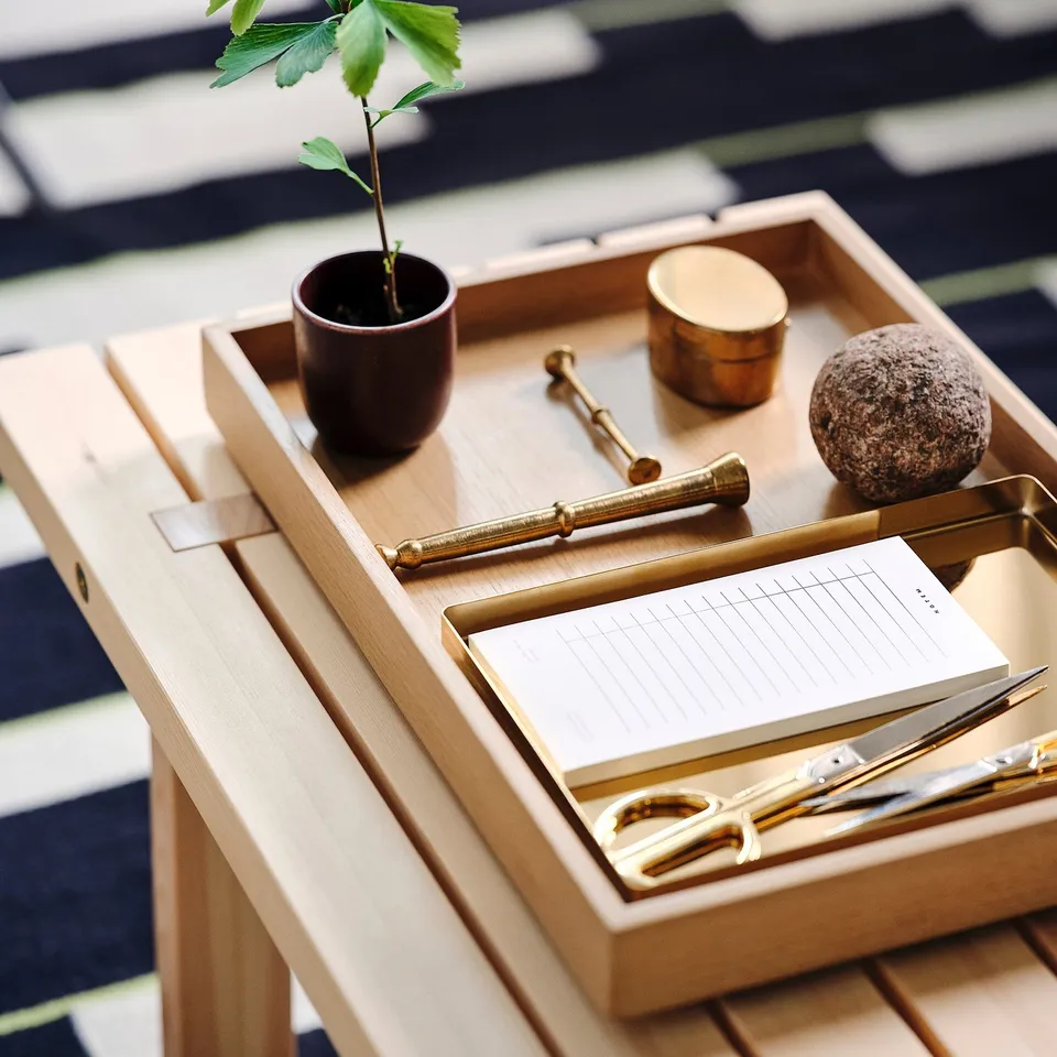 STOCKHOLM 2025 light oak tray holds items neatly. Small plant, gold pen, cup, rock, notebook, and scissors. Perfect for desktop organisation.